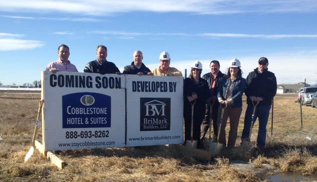 people with shovels in front of a sign at the ground breaking of the cobblestone inn and suites